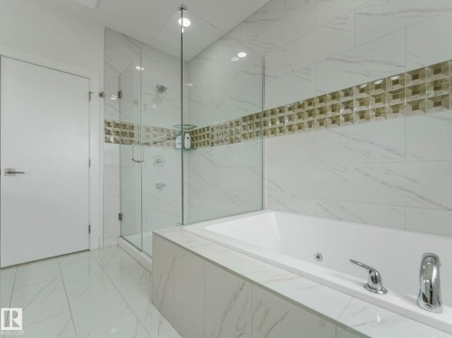 Soaking tub featuring chrome fixtures, full tile surround, walk-in shower with glass enclosure, white rectangular floor tiles, and a decorative tiled accent band - 3101 Pelerin Crescent, Beaumont, AB 
