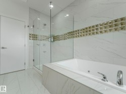 Soaking tub featuring chrome fixtures, full tile surround, walk-in shower with glass enclosure, white rectangular floor tiles, and a decorative tiled accent band - 