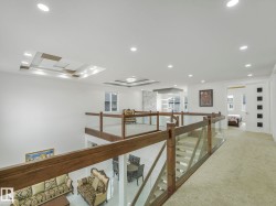 Upper-level landing featuring wood-finish and glass railings, recessed lighting, and a textured carpeted floor - 