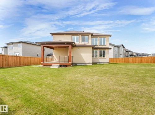 Expansive backyard featuring a manicured lawn, a full wooden privacy fence, and a covered back patio with glass panel railings - 3101 Pelerin Crescent, Beaumont, AB 