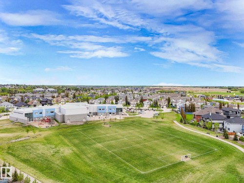 Expansive green space featuring a marked sports field, a nearby building with blue and gray facade elements, and a playground structure - 3101 Pelerin Crescent, Beaumont, AB 