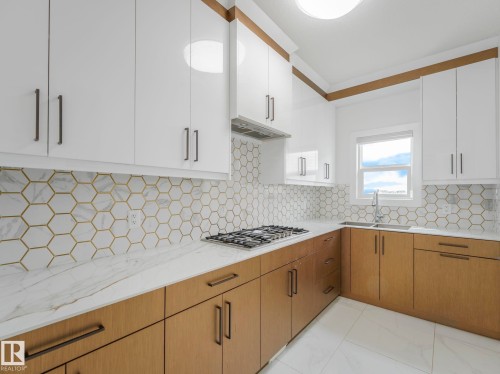 Contemporary kitchen featuring two-tone cabinetry with white upper cabinets and natural wood-finish lower cabinets, complemented by dark hardware - 3101 Pelerin Crescent, Beaumont, AB 