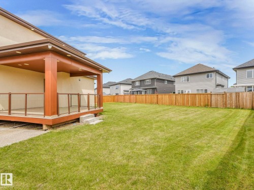 Expansive backyard featuring a covered deck with glass panel railings, a large manicured lawn, and a perimeter wood fence - 3101 Pelerin Crescent, Beaumont, AB 