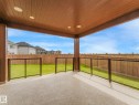 Covered patio featuring a durable stone-finish surface, wood-paneled ceiling with recessed lighting, and a glass-paneled railing - 3101 Pelerin Crescent, Beaumont, AB 