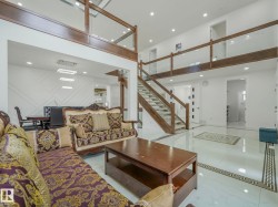 Bright interior with polished tile flooring, a prominent staircase with wood and glass railings, and a second-story open walkway - 