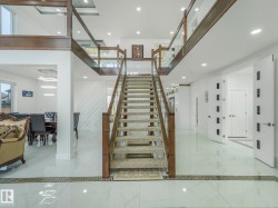 Grand foyer featuring a central staircase with wood-finish handrails and glass panels - 