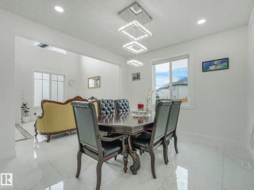Open-concept dining area featuring a modern rectangular chandelier, recessed lighting, and large windows - 3101 Pelerin Crescent, Beaumont, AB 