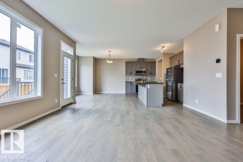 Expansive open-concept living area featuring wood-finish flooring, large windows, and a glass-paneled exterior door - 2031 207 Street, Edmonton, AB 