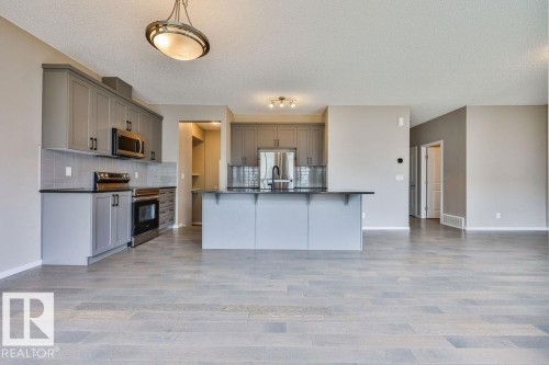 Spacious kitchen featuring gray cabinetry, stainless steel appliances, dark countertops, a tiled backsplash, and an island with bar seating - 2031 207 Street, Edmonton, AB 