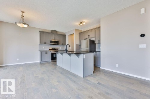 Modern kitchen featuring a central island with a matte black faucet, gray cabinetry, stainless steel appliances, and dark countertops - 2031 207 Street, Edmonton, AB 
