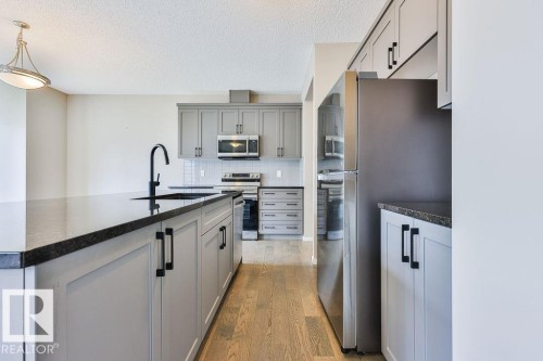 Kitchen featuring light gray cabinetry, dark countertops, wood-finish flooring, stainless steel appliances, and a white subway tile backsplash - 2031 207 Street, Edmonton, AB 