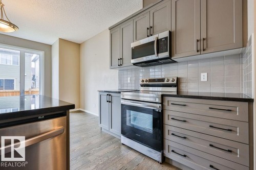Kitchen featuring gray cabinetry, stainless steel appliances, black countertops, a tile backsplash, and wood-finish flooring - 2031 207 Street, Edmonton, AB 