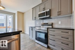 Kitchen featuring gray cabinetry, stainless steel appliances, black countertops, a tile backsplash, and wood-finish flooring - 