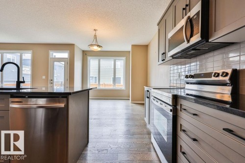 Kitchen featuring stainless steel appliances, dark countertops, gray cabinetry, and a tile backsplash - 2031 207 Street, Edmonton, AB 