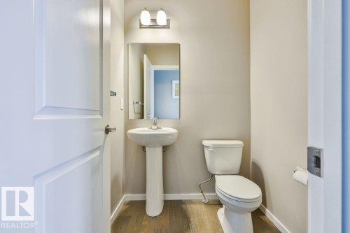 Powder room featuring a pedestal sink with chrome faucet, a rectangular wall-mounted mirror, and a two-light vanity fixture - 2031 207 Street, Edmonton, AB 