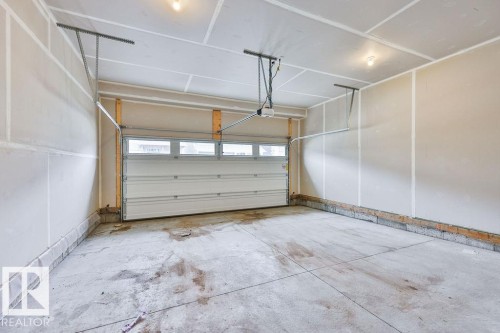 Spacious garage featuring a concrete floor, overhead lighting, and a paneled garage door with upper windows - 2031 207 Street, Edmonton, AB 