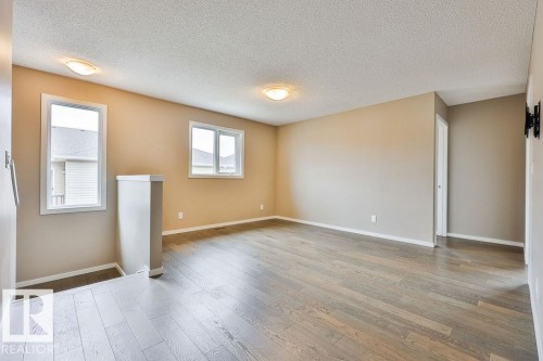 Spacious room featuring wood-finish flooring, neutral-toned walls, multiple windows, and ceiling-mounted light fixtures - 2031 207 Street, Edmonton, AB 