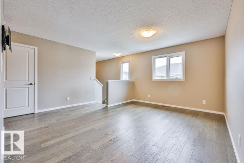 Spacious room featuring light wood-finish flooring, neutral wall paint, white trim, and multiple windows - 2031 207 Street, Edmonton, AB 