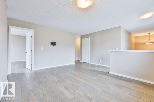 Spacious room featuring wood-finish flooring, neutral-toned walls, and recessed ceiling lighting - 2031 207 Street, Edmonton, AB 