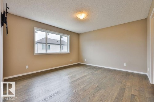Spacious room featuring wood-finish flooring, neutral wall paint, and a large window - 2031 207 Street, Edmonton, AB 
