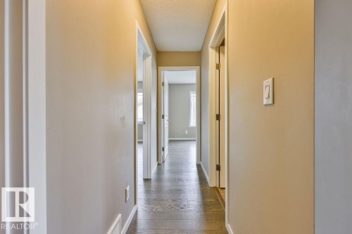 Hallway with wood-finish flooring, light neutral-toned walls, white trim, and multiple doorways - 2031 207 Street, Edmonton, AB 