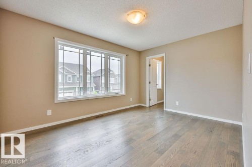 Spacious interior room featuring wood-finish flooring, a large multi-pane window with white trim, a flush-mount ceiling light, and neutral wall paint - 2031 207 Street, Edmonton, AB 