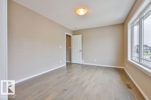 Spacious room featuring light-toned walls, wood-finish flooring, and a large multi-pane window - 2031 207 Street, Edmonton, AB 