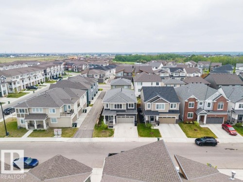 Aerial perspective showcasing a residential community with diverse architectural styles, featuring two-story homes with attached garages, shingled roofs, and varied exterior finishes including brick, siding, and stone accents - 2031 207 Street, Edmonton, AB 