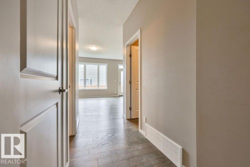 Hallway featuring rich wood-finish flooring, light neutral wall tones, and recessed baseboard heating - 2031 207 Street, Edmonton, AB 