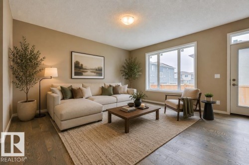 Bright living room featuring wood-finish flooring, a large multi-pane window, and a glass-paneled exterior door. Virtually Staged Photos - 2031 207 Street, Edmonton, AB 