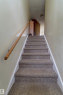 Carpeted staircase with a natural wood handrail, leading to an upper level with light-toned walls and ceiling - 