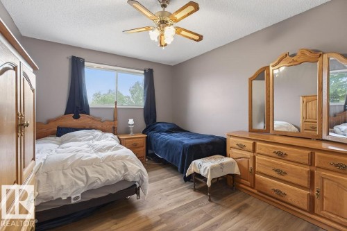 Bedroom featuring wood-finish flooring, a window with exterior tree scenery, a ceiling fan with integrated lighting, and neutral wall paint - 123 Grandin Drive, Morinville, AB 