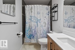 Bathroom featuring a white vanity with an integrated sink and wood-finish cabinetry, dark tiled shower surround, and black fixtures - 