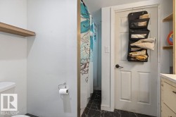 Bathroom featuring a white paneled door with matte black hardware, dark stone-finish flooring, a white toilet, and a wood-finish floating shelf - 