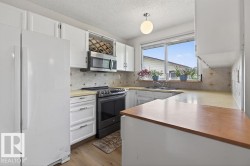 Kitchen featuring white cabinetry, integrated wine rack, stainless steel over-the-range microwave, wood-finish flooring, and a large window above the sink - 