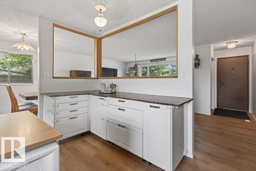 White cabinetry with dark countertops, wood-finish flooring, and a pass-through window with wood trim - 123 Grandin Drive, Morinville, AB 