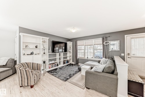 Living area featuring light wood-finish flooring, built-in shelving, a large window with blinds, and a built-in entertainment center - 53 150 Edwards Drive, Edmonton, AB 