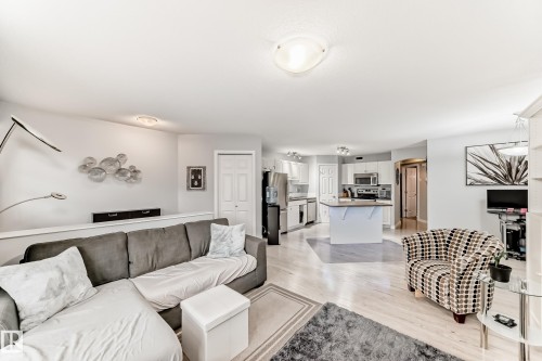 Open-concept living space featuring wood-finish flooring, recessed lighting, white walls, and a kitchen with white cabinetry and stainless steel appliances - 53 150 Edwards Drive, Edmonton, AB 