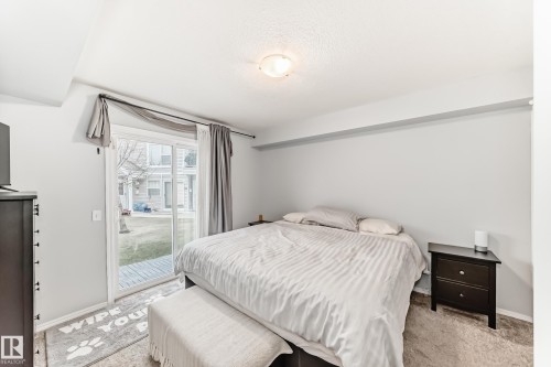 Bedroom featuring a sliding glass door providing direct outdoor access, carpet flooring, a flush-mount ceiling light fixture, and light-toned walls - 53 150 Edwards Drive, Edmonton, AB 