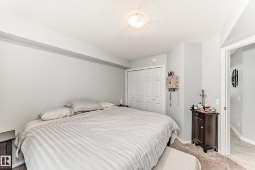Recessed lighting and a flush-mount ceiling light illuminate this bedroom, featuring light gray wall tones and a textured ceiling - 53 150 Edwards Drive, Edmonton, AB 