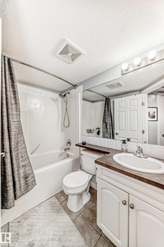 Bathroom featuring a white bathtub with shower, toilet, and vanity with an integrated sink - 53 150 Edwards Drive, Edmonton, AB 
