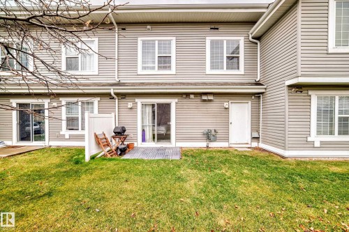 Rear exterior featuring horizontal siding, multiple windows with white trim, and a sliding glass door opening to a ground-level patio area - 53 150 Edwards Drive, Edmonton, AB 