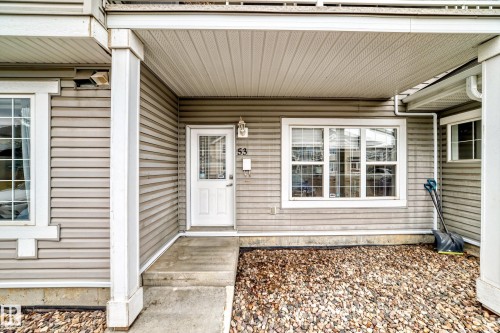 Front entry featuring a white door with upper glass panel, an exterior light fixture, and a house number - 53 150 Edwards Drive, Edmonton, AB 
