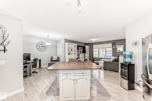 Open-concept interior featuring light wood-finish flooring, a kitchen island with white cabinetry, built-in shelving, and recessed lighting - 53 150 Edwards Drive, Edmonton, AB 