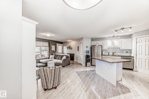 Open-concept living space featuring wood-finish flooring, a kitchen island with a wood-finish countertop, white cabinetry, stainless steel appliances, and track lighting - 53 150 Edwards Drive, Edmonton, AB 