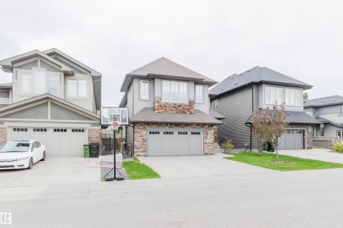 Modern multi-level residence featuring a two-car garage, gray siding, stone accents, and a paved driveway - 1957 Ainslie Link, Edmonton, AB 