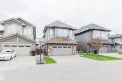 Modern multi-level residence featuring a two-car garage, gray siding, stone accents, and a paved driveway - 