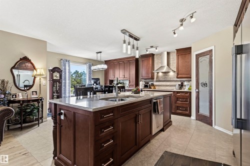 Open-concept kitchen featuring an oversized island with an undermount sink, recessed panel cabinetry, stainless steel appliances, a tile backsplash, and ceramic tile flooring - 32 Lamplight Bay, Spruce Grove, AB 