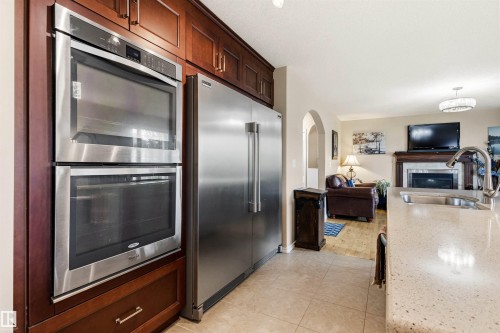 Kitchen appliances featuring stainless steel double ovens and a full-size refrigerator, complemented by rich wood cabinetry - 32 Lamplight Bay, Spruce Grove, AB 
