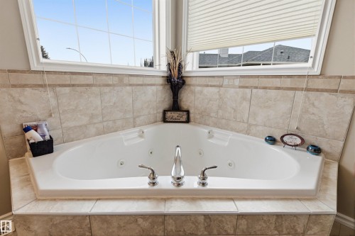 Corner jetted tub with polished chrome fixtures, surrounded by neutral-toned tiled surfaces - 32 Lamplight Bay, Spruce Grove, AB 